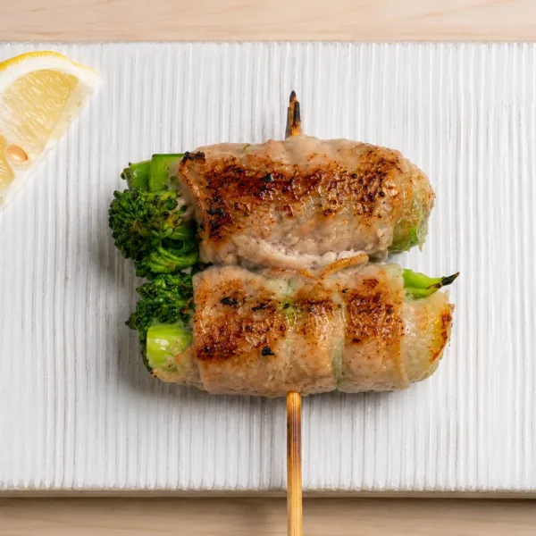 Pork-wrapped baby broccoli skewer served with grilled vegetables and lemon